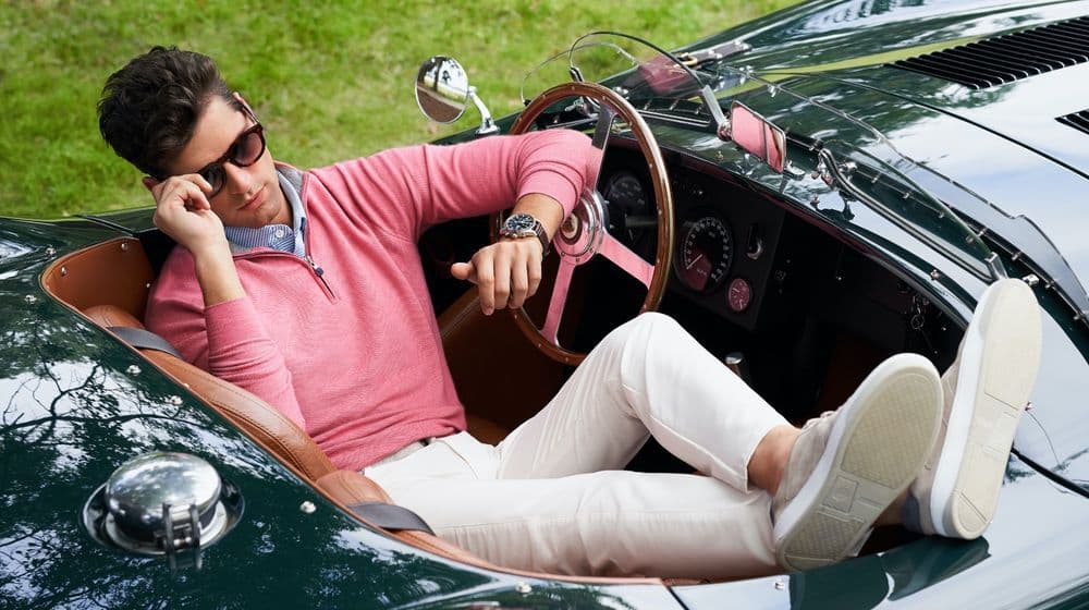 a man in a pink quarter-zip lounging in a vintage green convertible